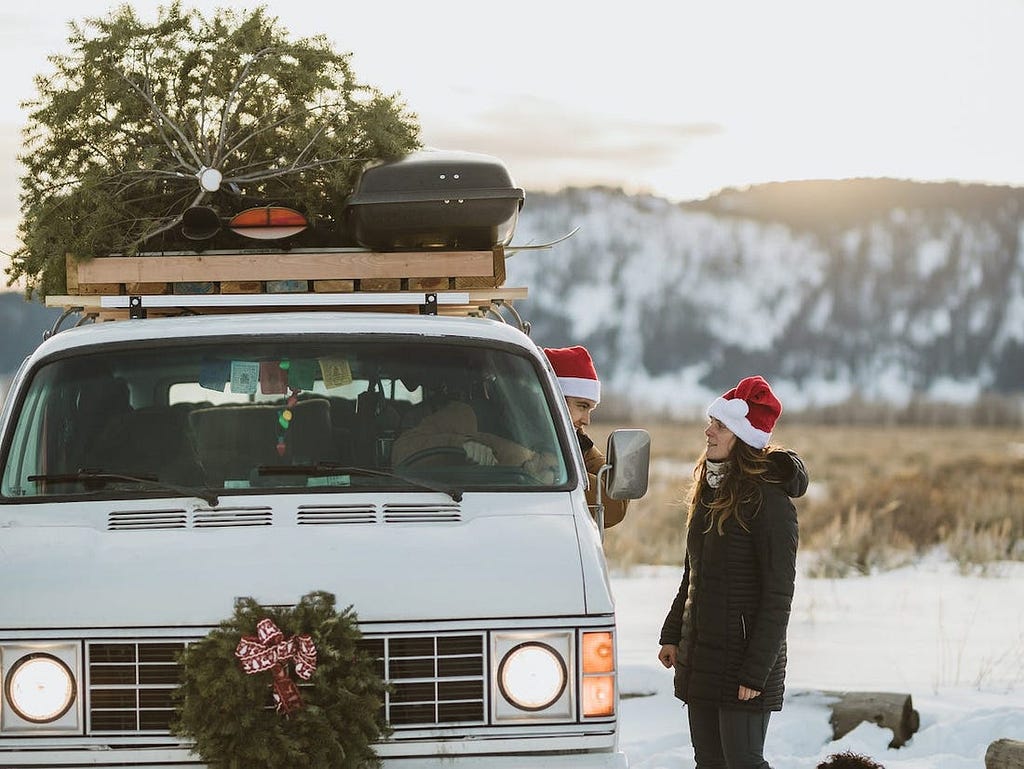 A couple wears Christmas hats outside their van.