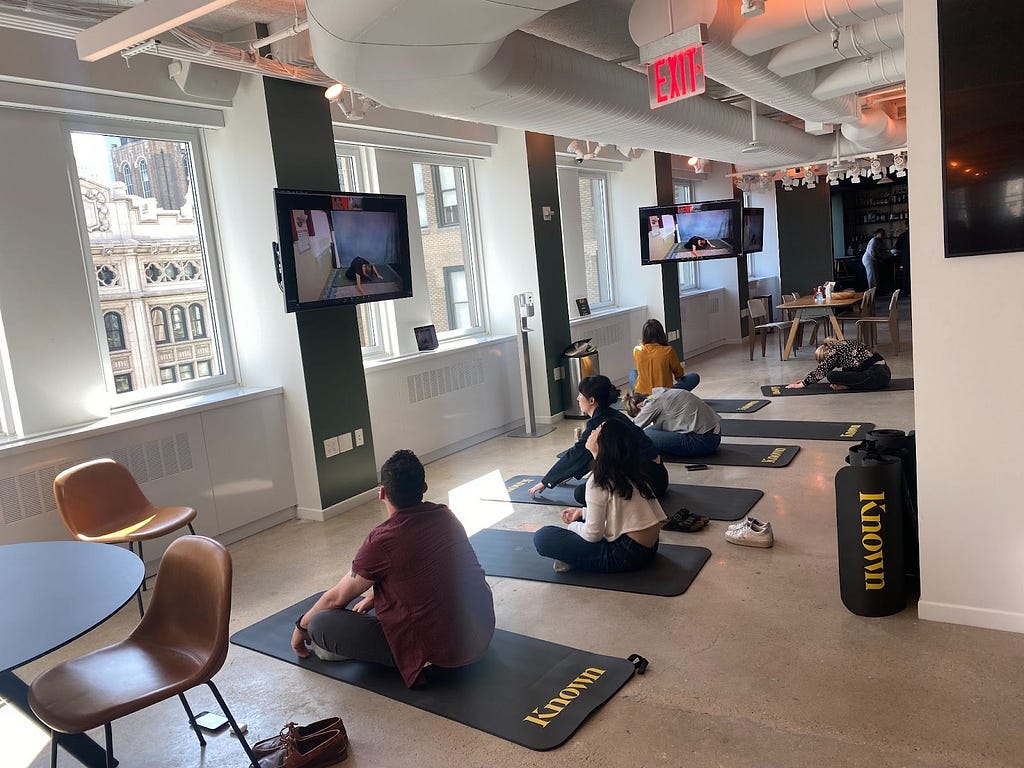 A photo of Known employees sitting on fitness mats as they attend a guided stretching session as part of Mental Health Awareness Month.