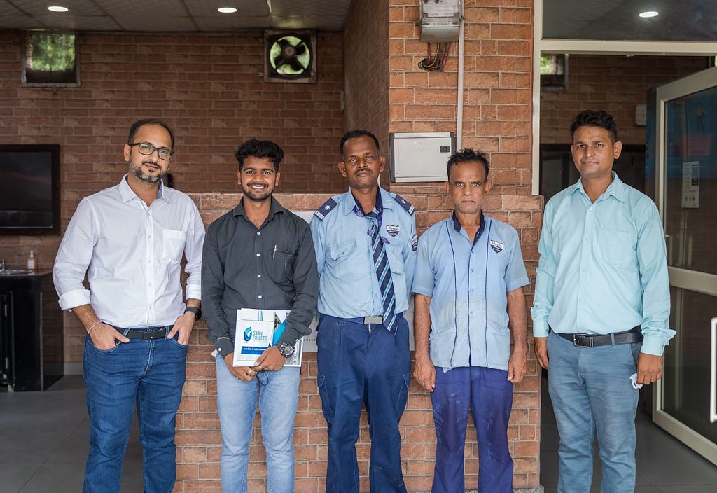 Group of 5 male individuals standing inside a public restroom center.