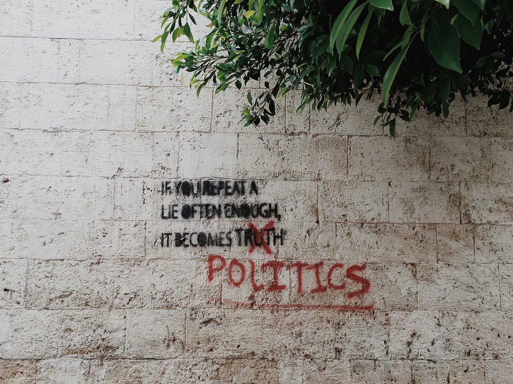 Graffiti on a wall. “If you repeat a lie often enough, it becomes truth” but with truth crossed out and replaced with “politics”.