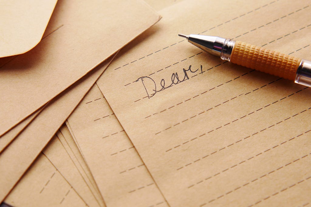 Sand-colored stationery, with “Dear” written at the top of a page and a pencil sitting beside the word