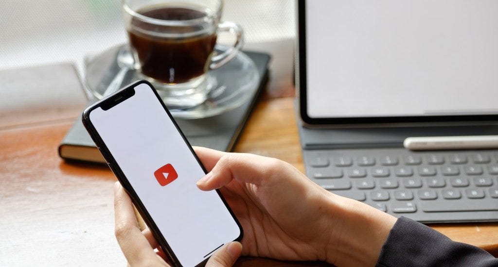A person holding a smartphone with the Youtube logo on the screen