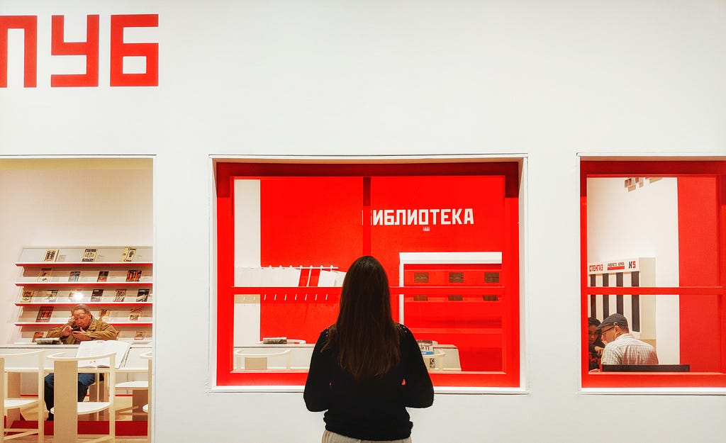 A woman stands in front of a bright red window inside a gallery shop.