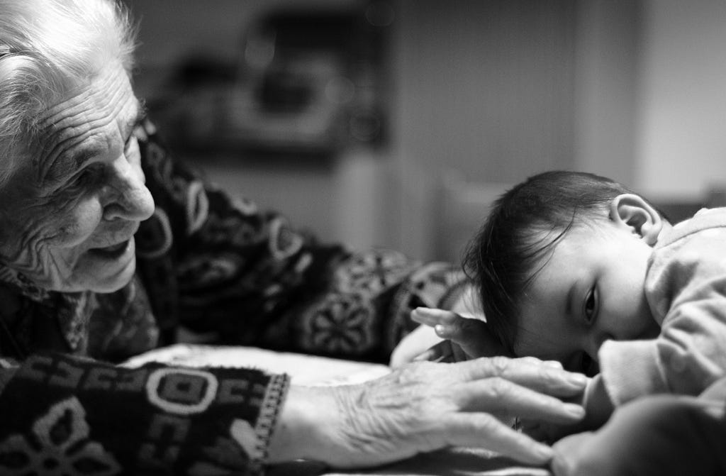 An elderly woman reaches out to a sleepy baby.