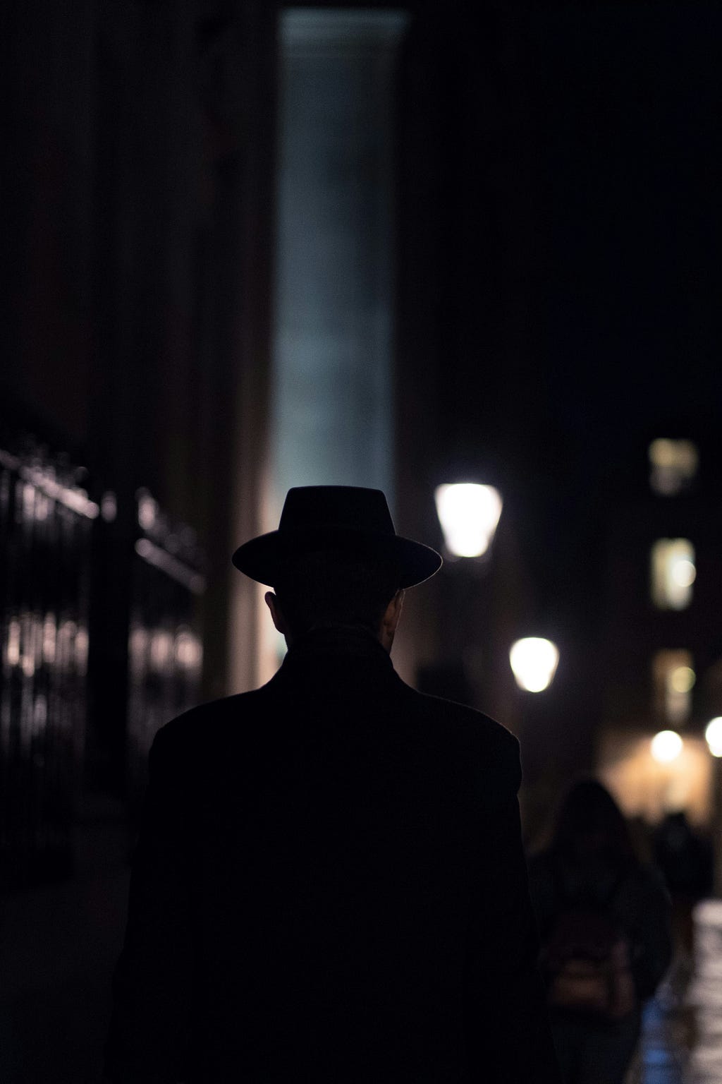 Man with fedora hat in the darkness surrounded by the city lamps.