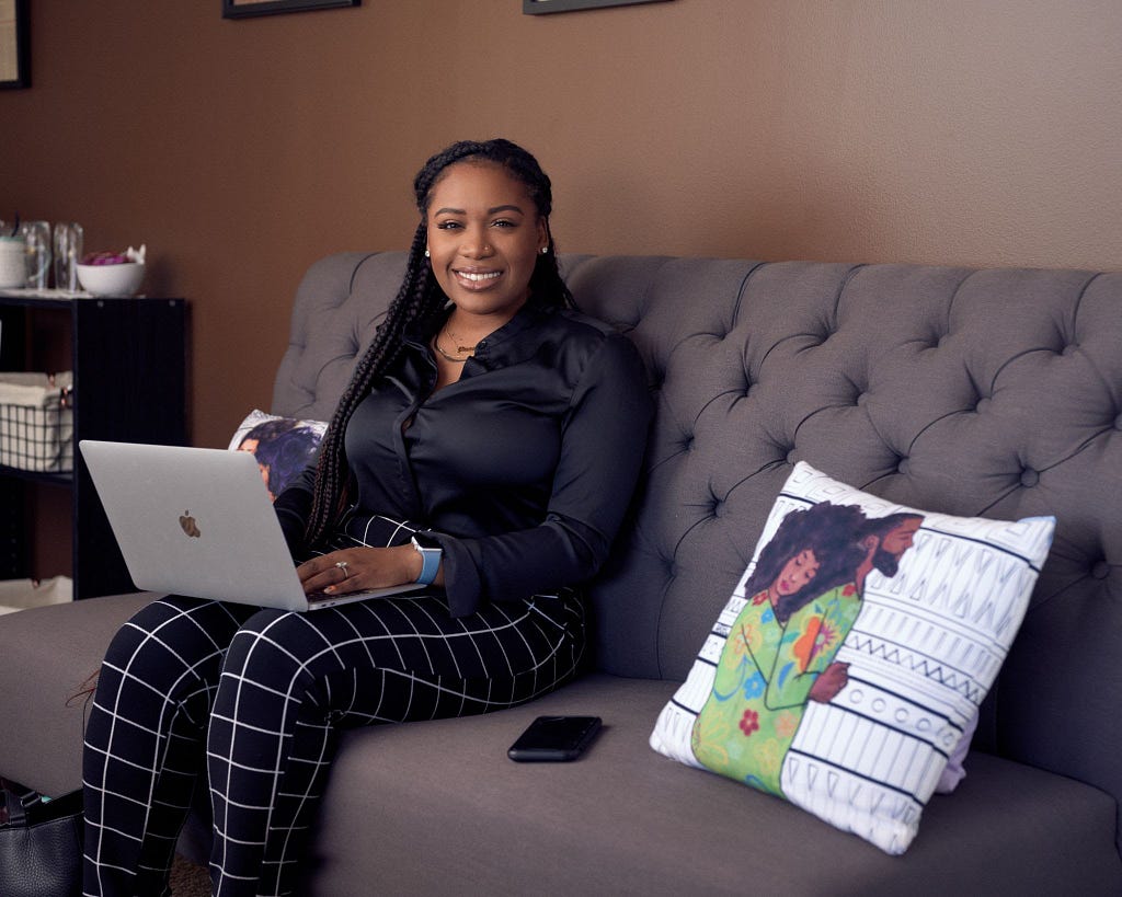 Aneese Johnson sitting on a grey couch while working on her laptop.
