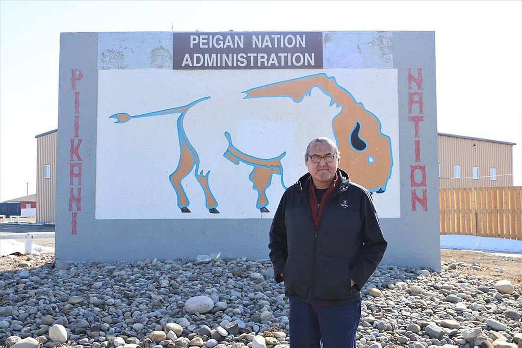 Ira standing in front of the Piikani First Nation’s Administration sign.