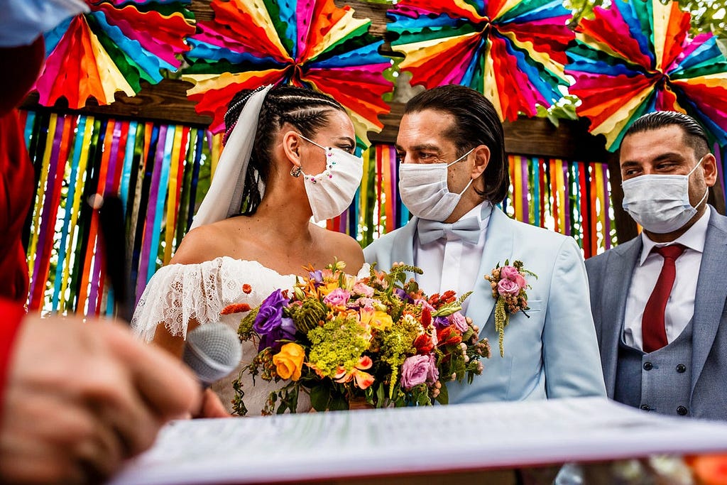 A bride and groom smile at one another while wearing masks.