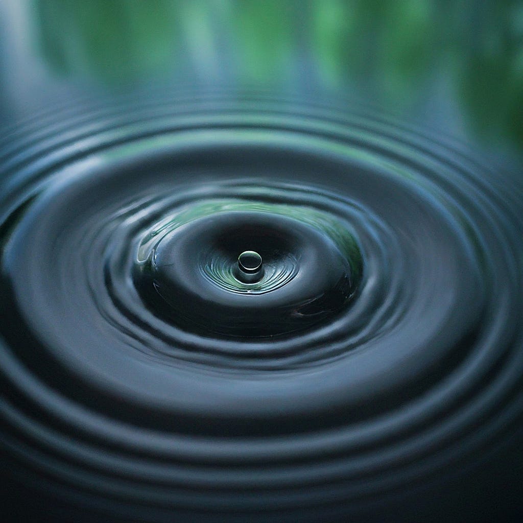 Close-up view of a water droplet impacting the surface of a body of water, creating concentric ripples, symbolizing the ripple effect of individual actions on environmental sustainability.