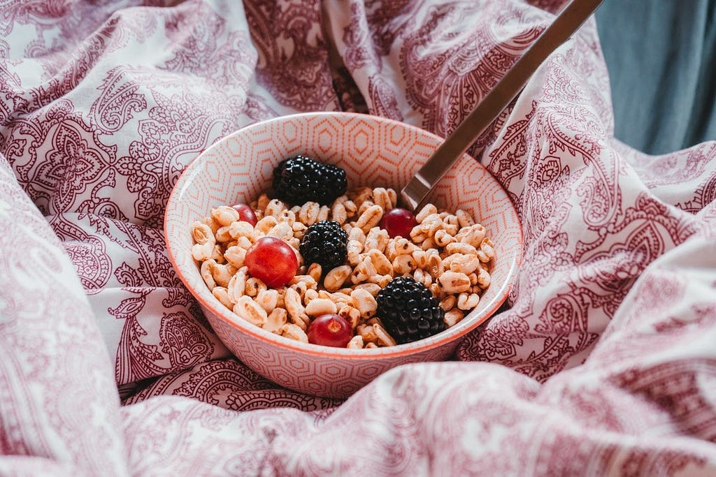 Bowl of cereal with berries and a spoon on a cozy comforter