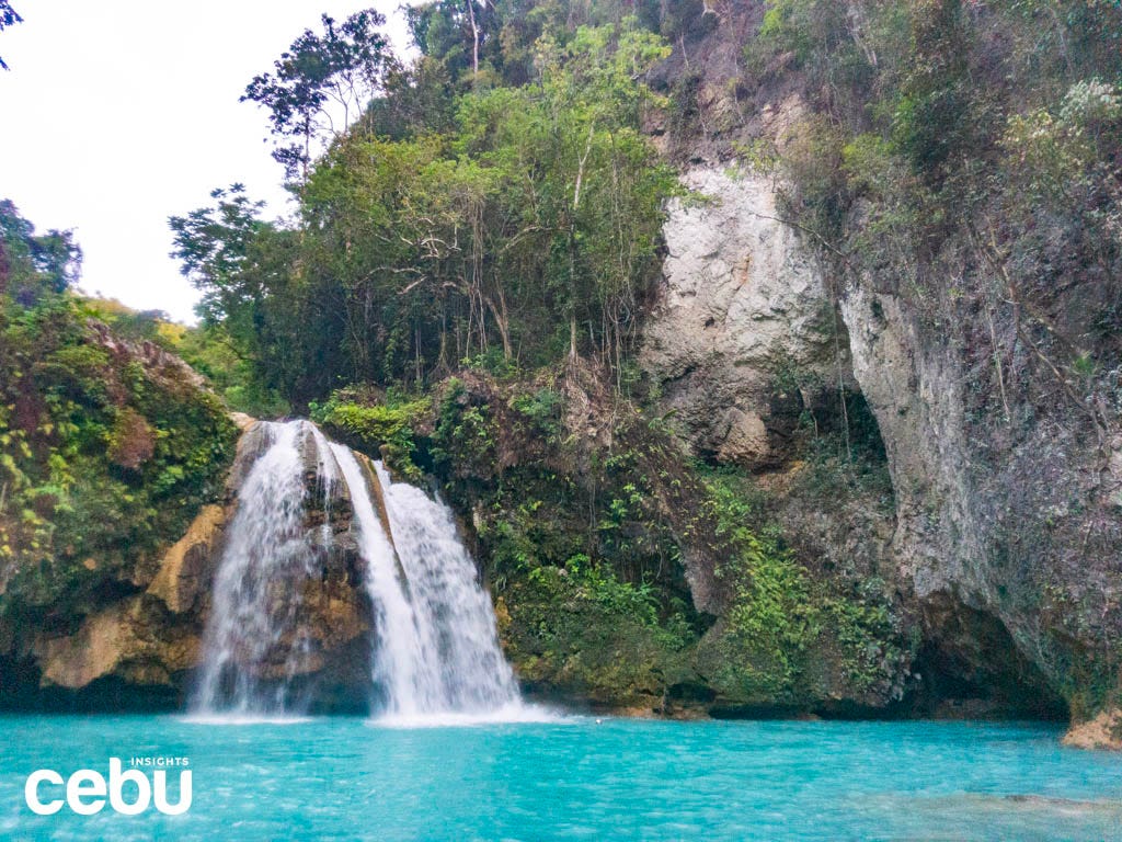 Wide shot of the Kawasan Falls surrounded by rocks and leaves