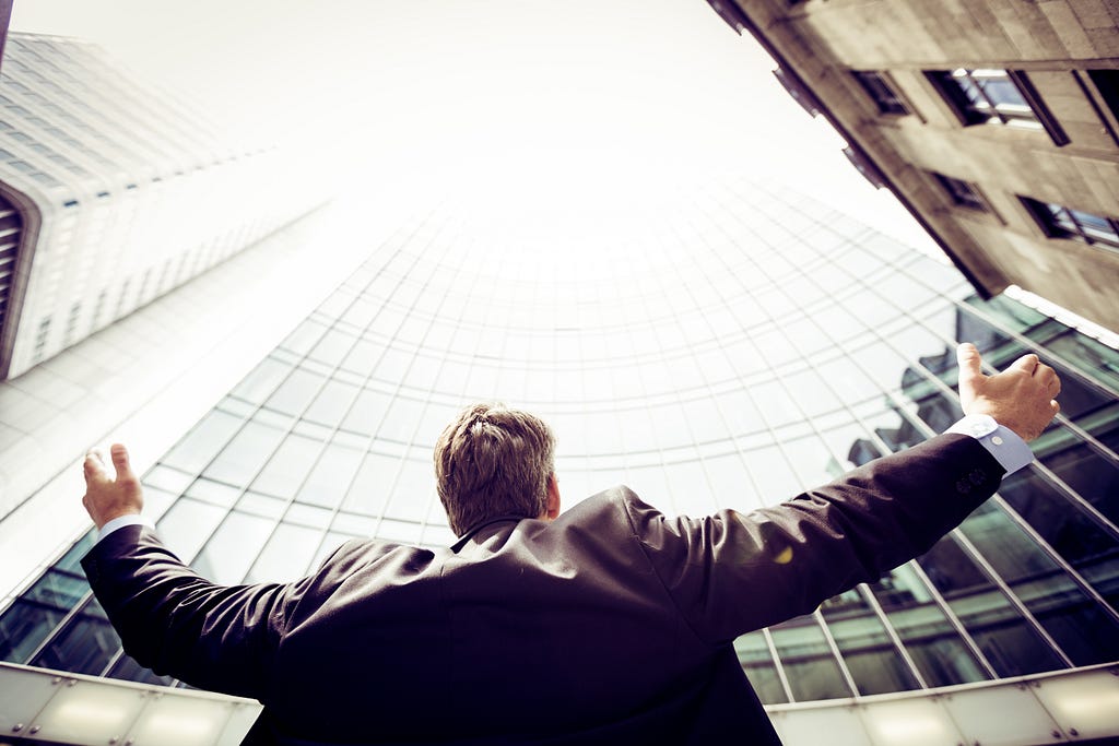 A man is looking up at the tall buildings above him, opening his arms toward the sky.