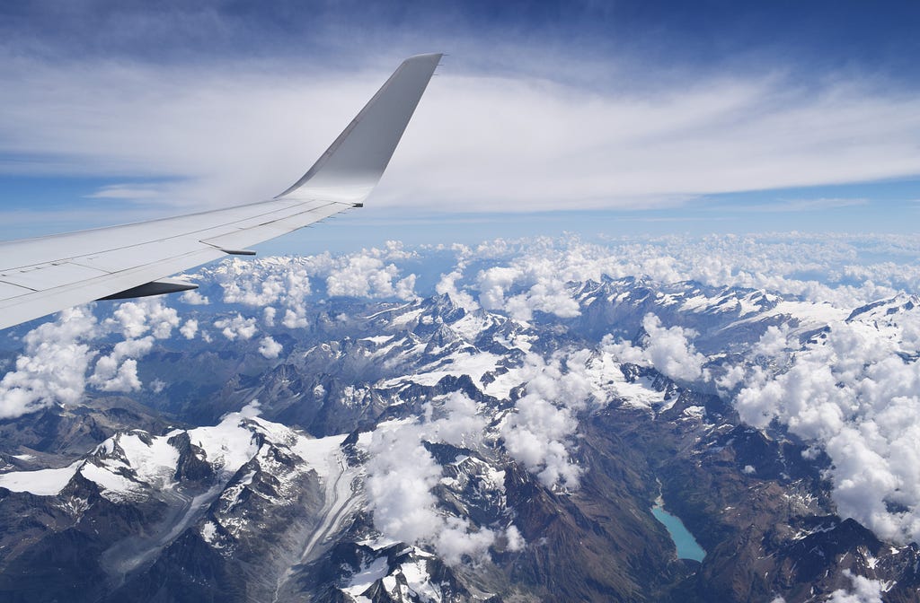 Airplane wing above clouds and mountains