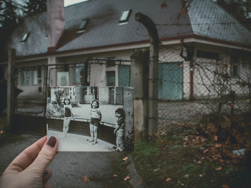 An old photograph of children in front of a house is held up in front of the same house in the present.