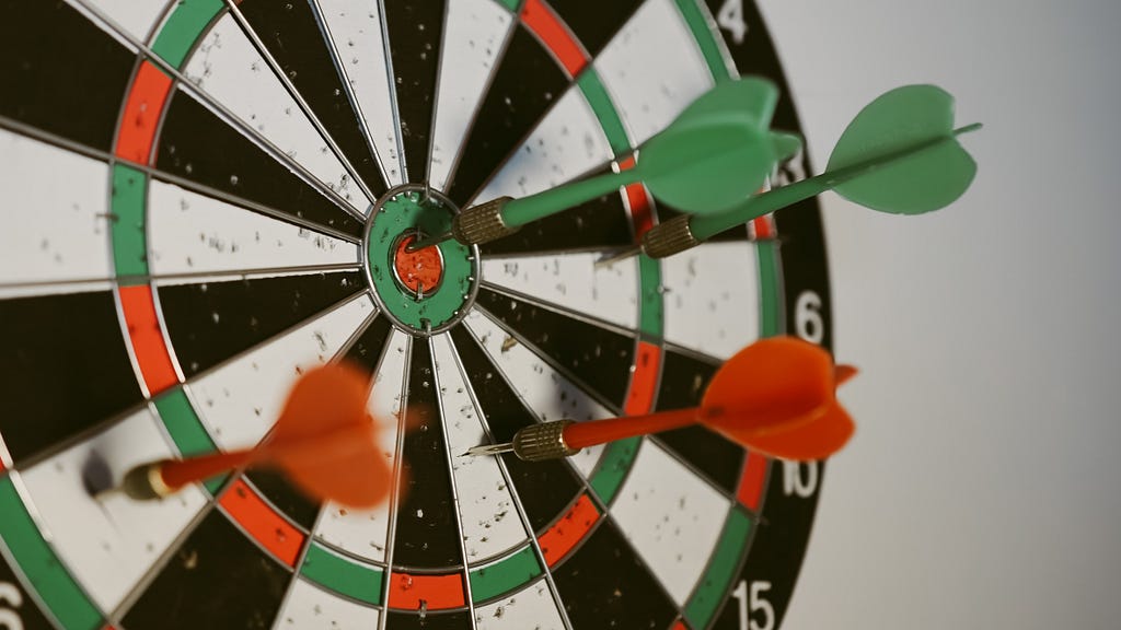 A dartboard with four darts are scattered around the center and only one is on the center.