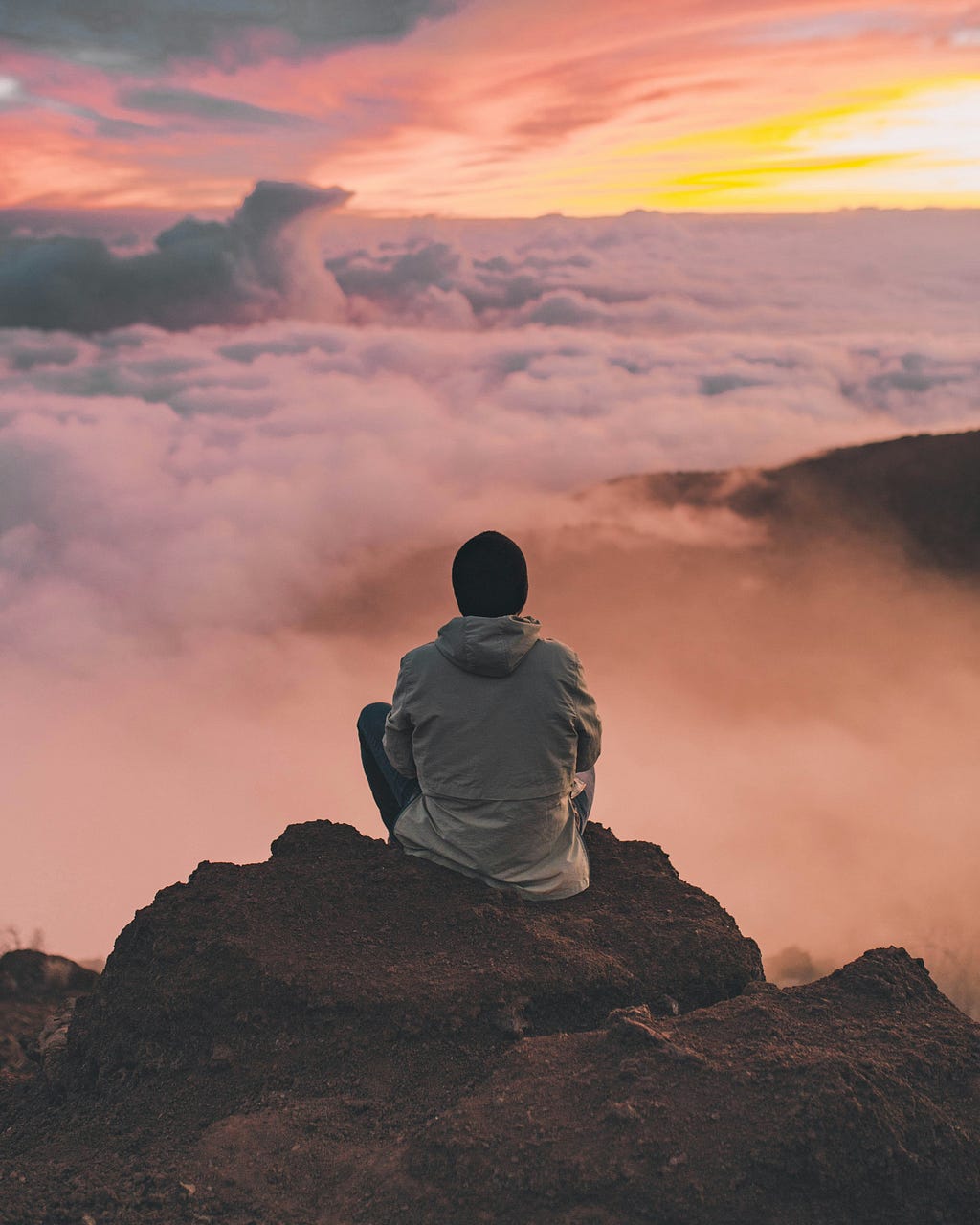 Human sitting on a mountain lookout gazing at the misty cloudy valley.