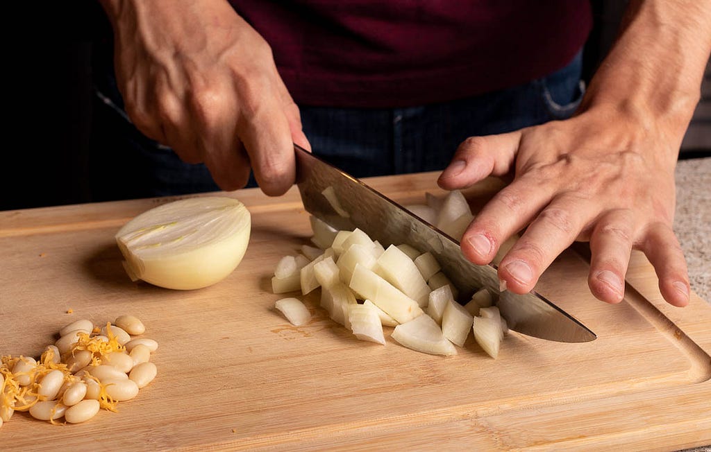 Man chopping onions with a chef’s knife on a wood cutting board.
