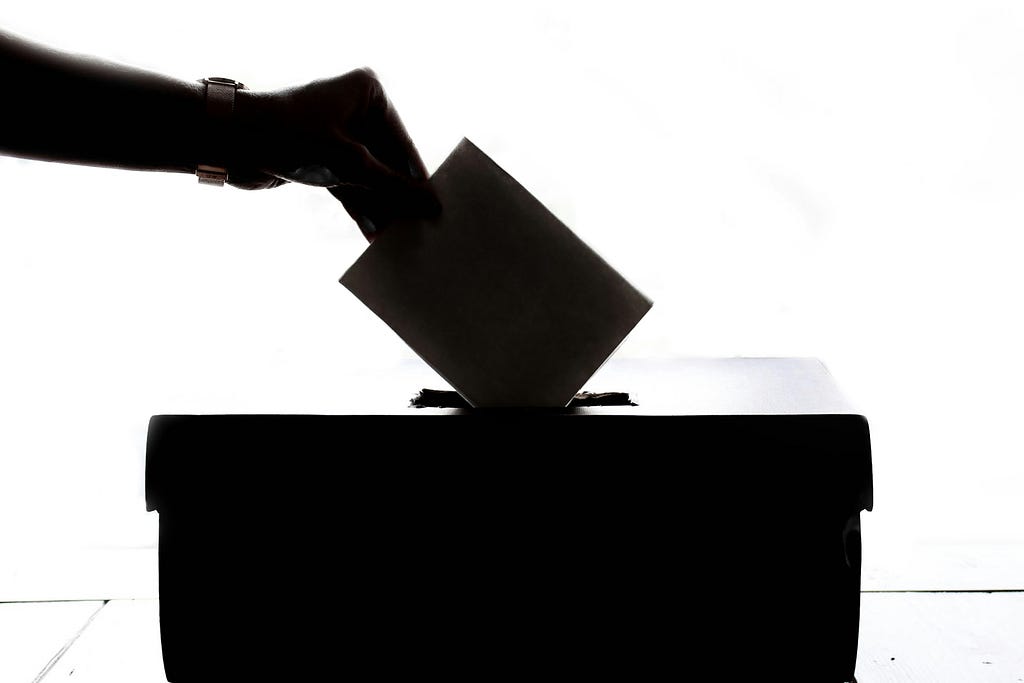 Black and white image of someone placing a paper ballot into a ballot box.