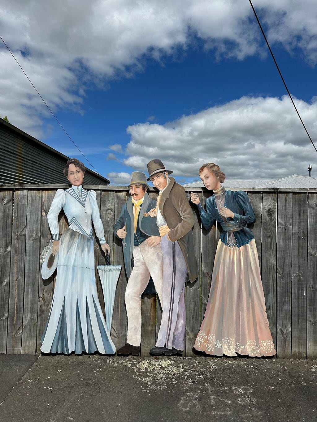 Wooden fence with cutout painted characters from turn of the century in Victorian dress.