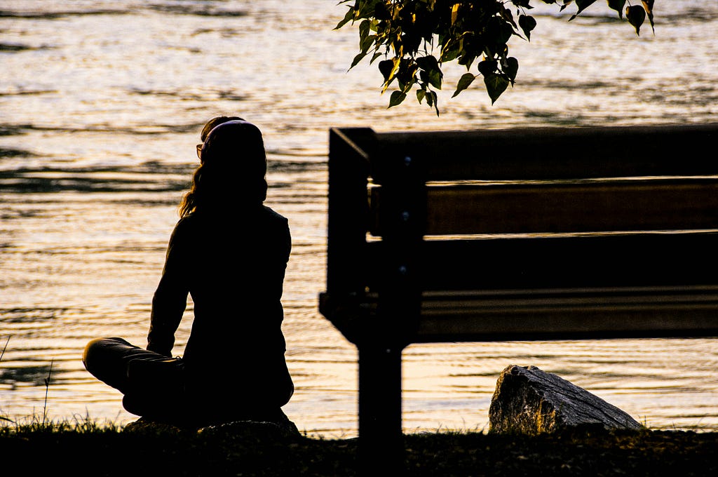 photograph at sunset of someone sitting on a rock next to a bench staring out at a peaceful lake