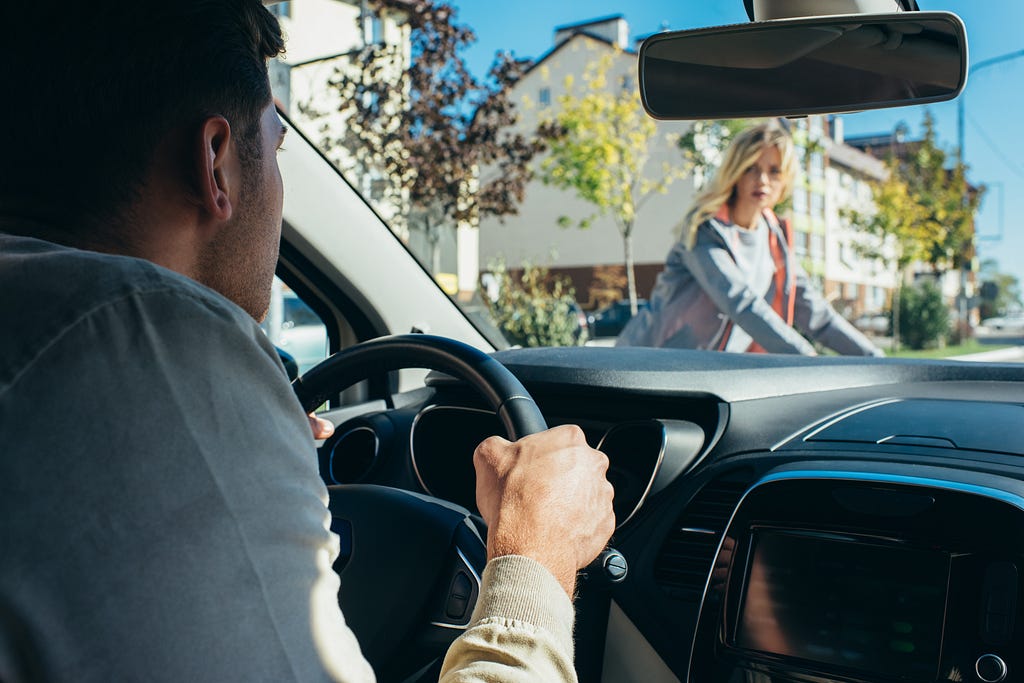 A man driving a car while a woman is crossing the road.