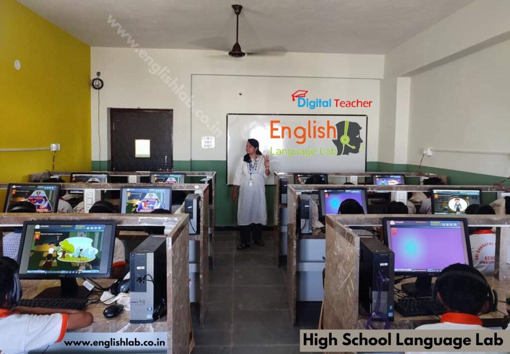 Students sit at computer equipment in an English language laboratory, with a large screen showing the ‘English Language Lab’ and a teacher nearby.