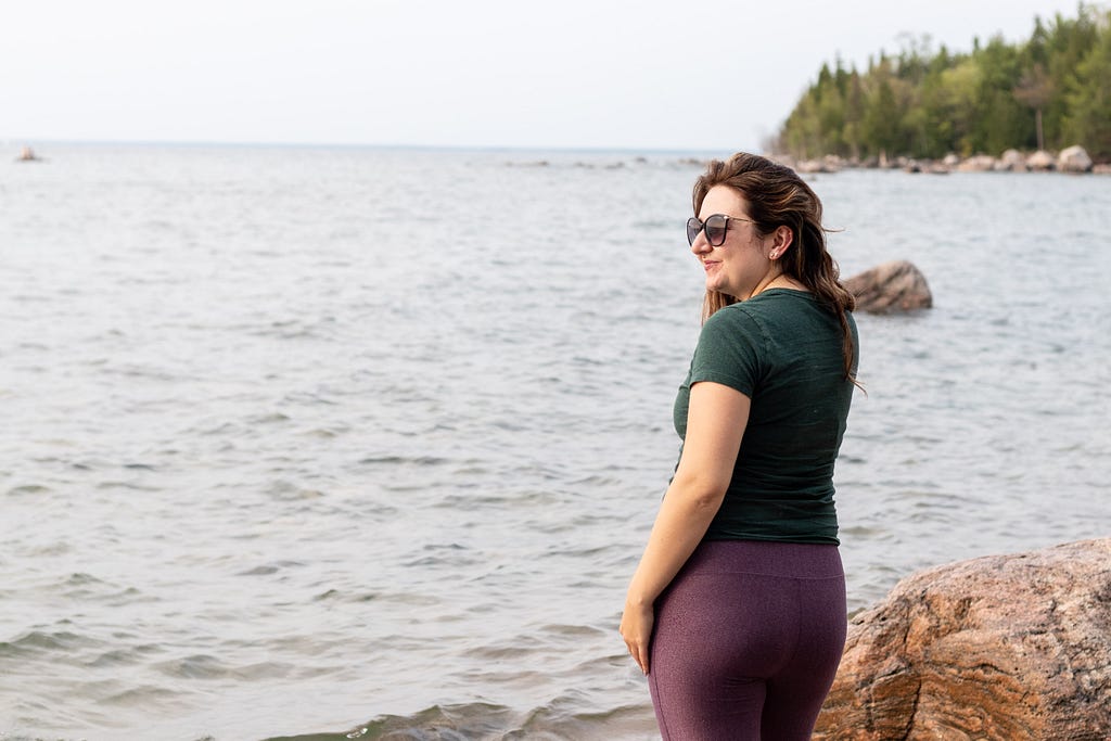 A photo of Sierra wearing purple leggings and a green shirt looking our at the water.
