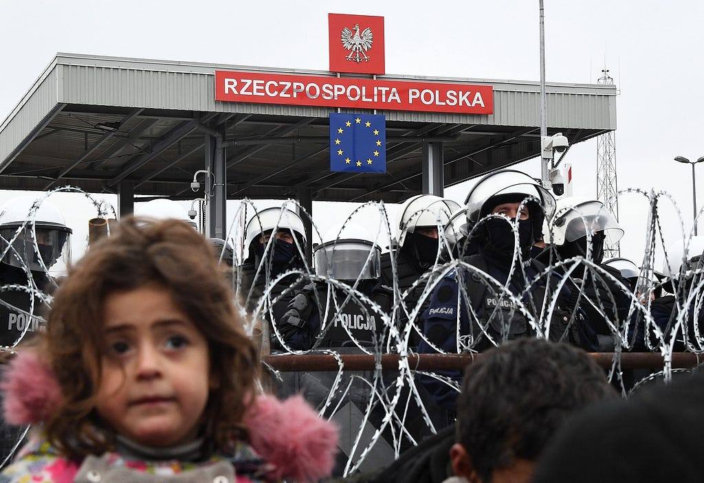 A girl stands next to the Belarusian fence as several Polish police officers stand guard at the Bruzgi-Kuznica Bialostocka border crossing, near the Belarusian-Polish border, on November 15, 2021, in Bruzgi, Belarus. thousands of people seeking to continue their advance towards the European Union have been crowding in, where in addition to living in the cold and in the open, attacks and altercations are taking place. Viktor Tolochko/Sputnik (Europa Press via AP)