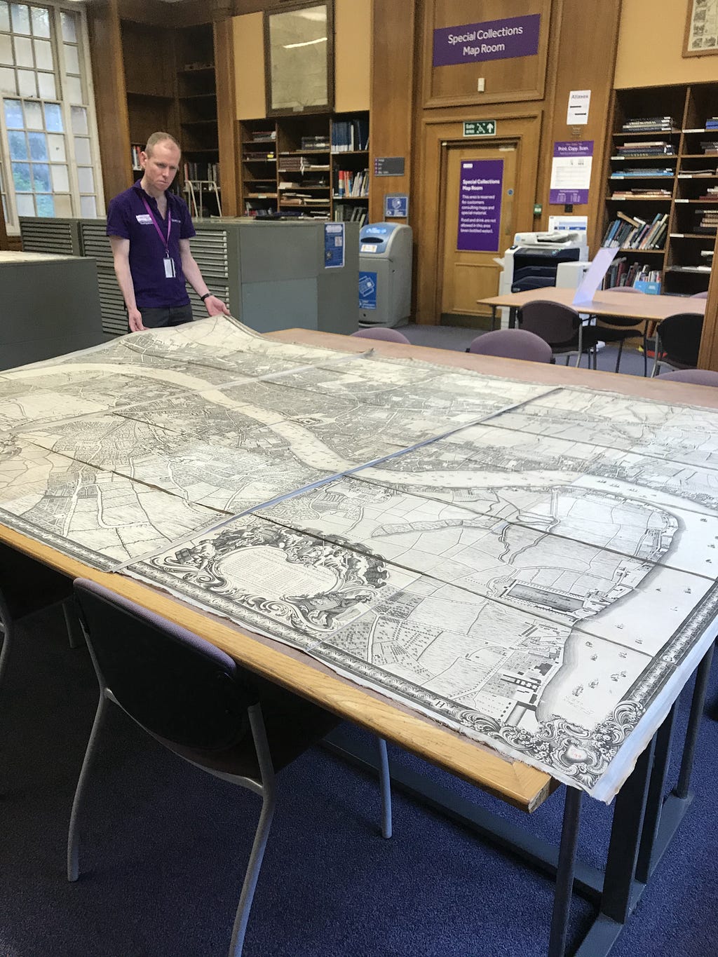 View of the map room at the University of Manchester Library. A member of Reader Services staff is opening up a very large antique map of London