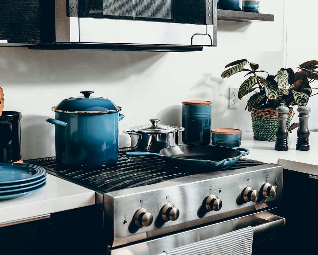 Pots and pans on a stovetop. A plant on a counter.