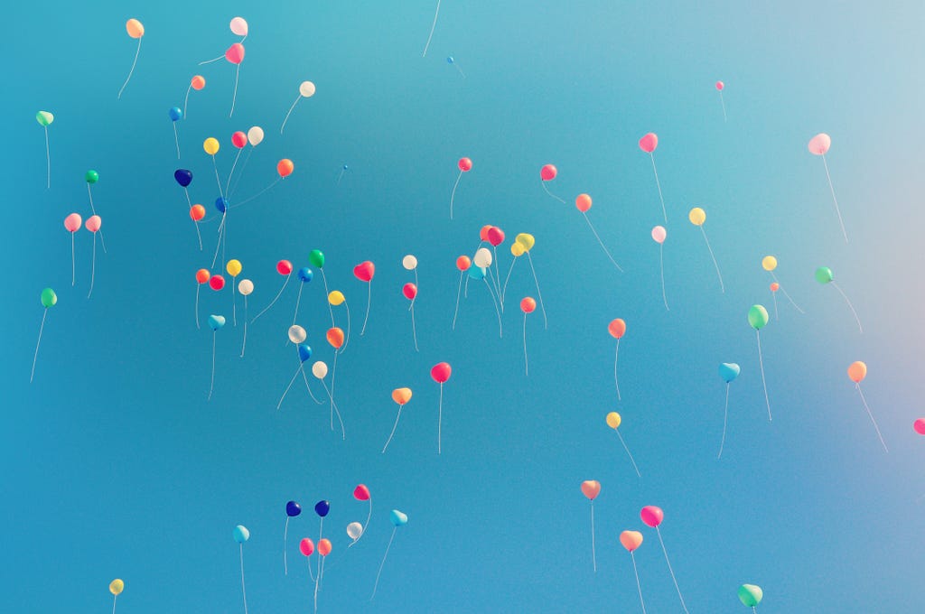 A true flock of multicolored balloons floating into a blue sky.