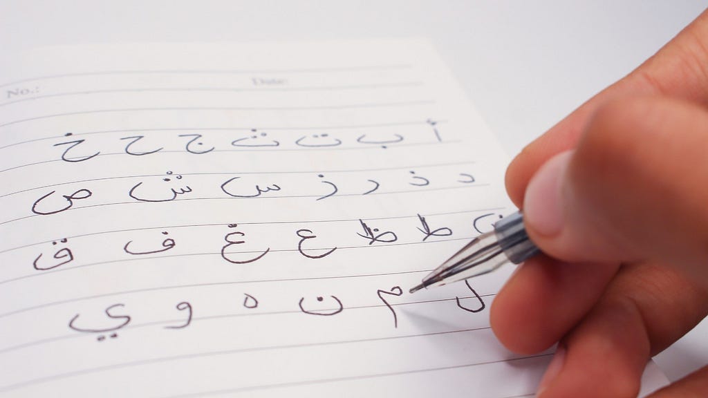 Close-up of a hand writing Arabic with a pencil. Photo by Indah Wahyuning Aprilia/Getty Images