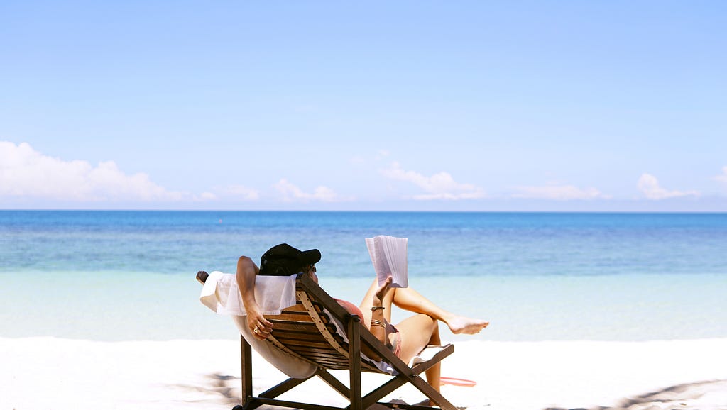 a woman reading a book while lying on a beach