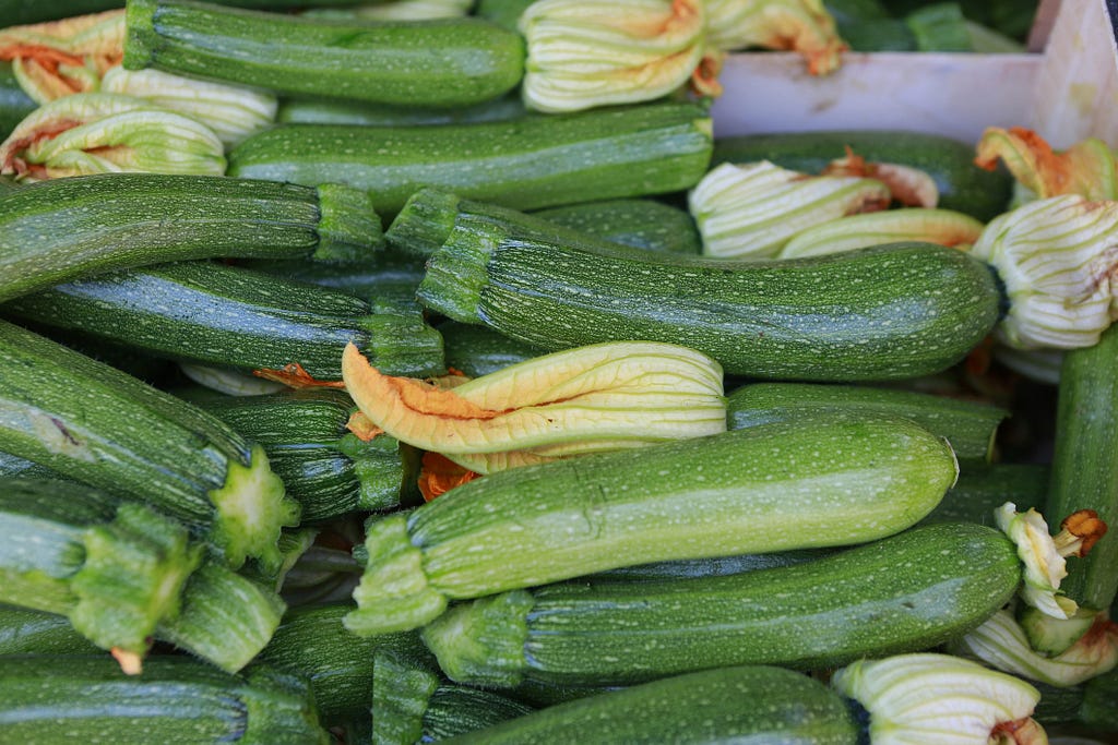 Closeup of stacks of zucchini with their flowers still attached for sale at a produce market.