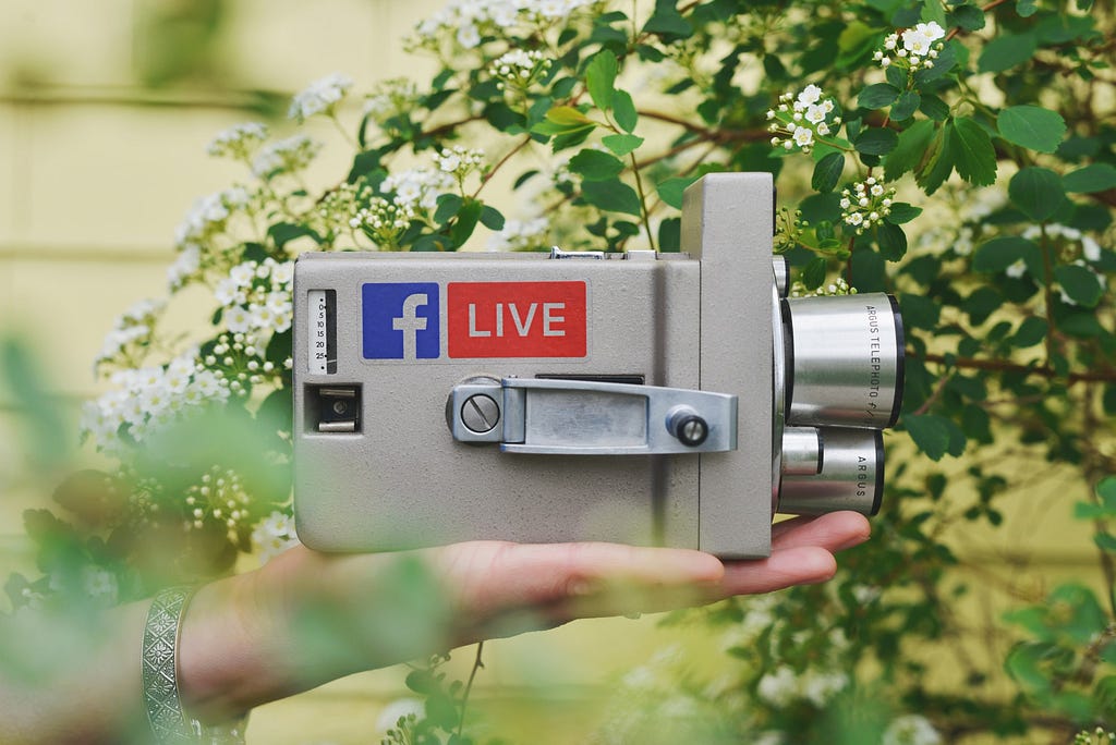 hand holding an old video camera with facebook logo sticker and red live sticker on the side