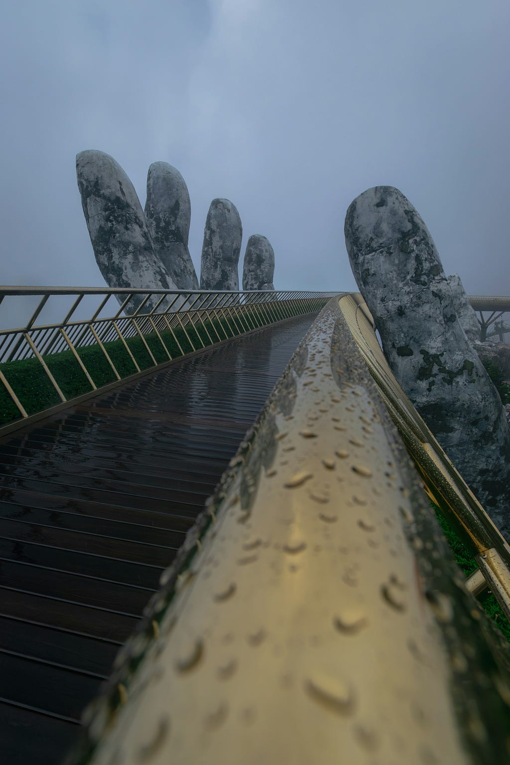 A wet bridge held up by a massive hands leading into the mist.