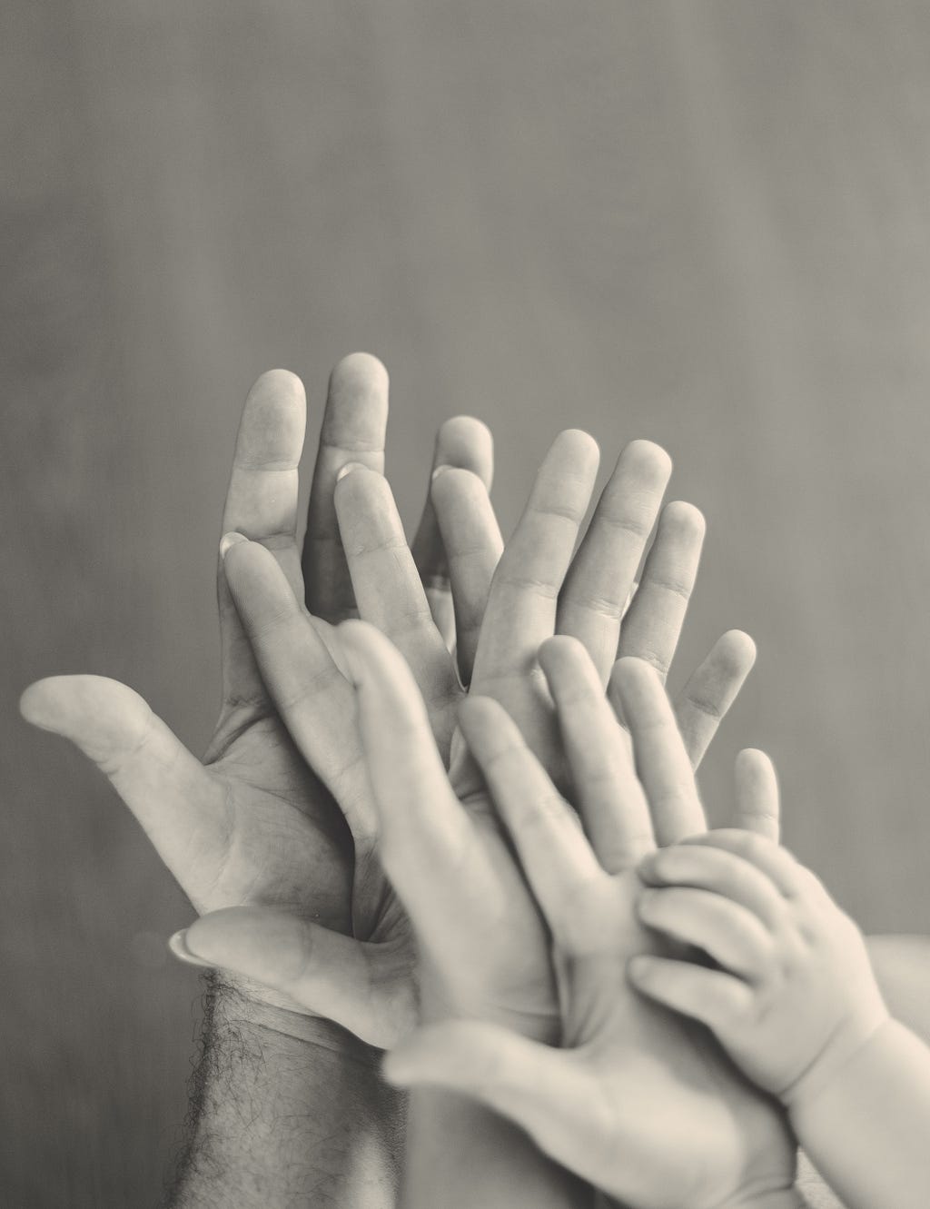 A black and white shot of five hands in varying sizes, depicting caregivers and their child.