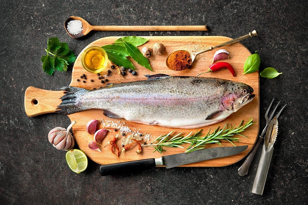 fish on a cutting board surrounded by spices like garlic, lime, rosemary, and chili