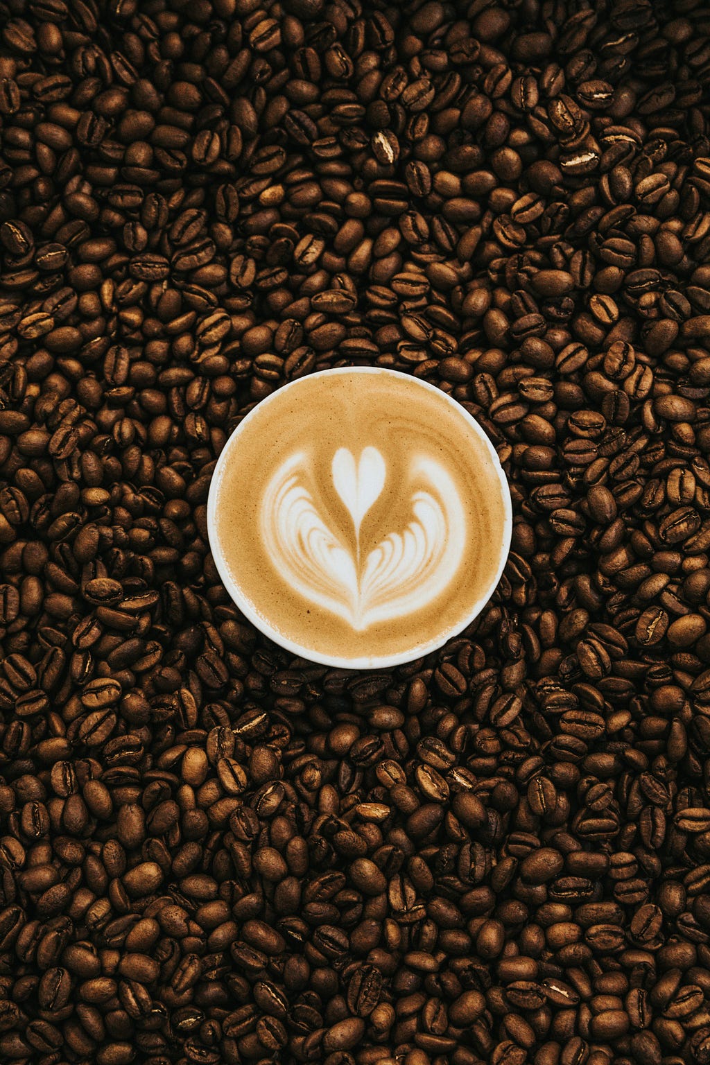 A cafe latte with heart-shaped latte art surrounded by coffee bans