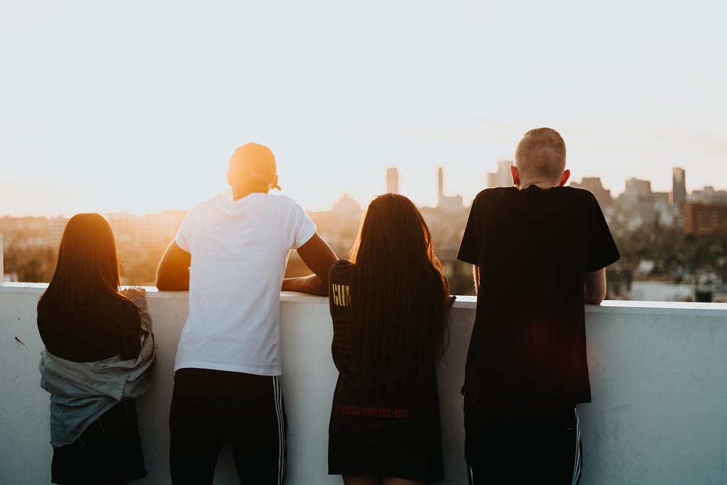 Two young men and two young women standing on the rooftop facing the sunset