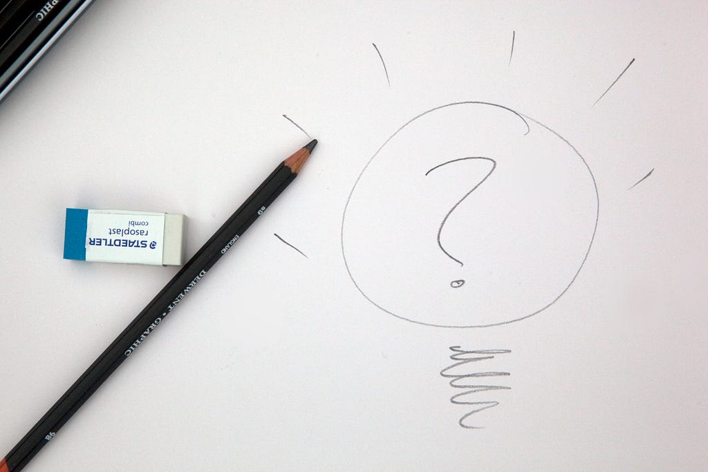 White paper with a pencil drawing of a lightbulb with a question mark inside and rays from the bulb.