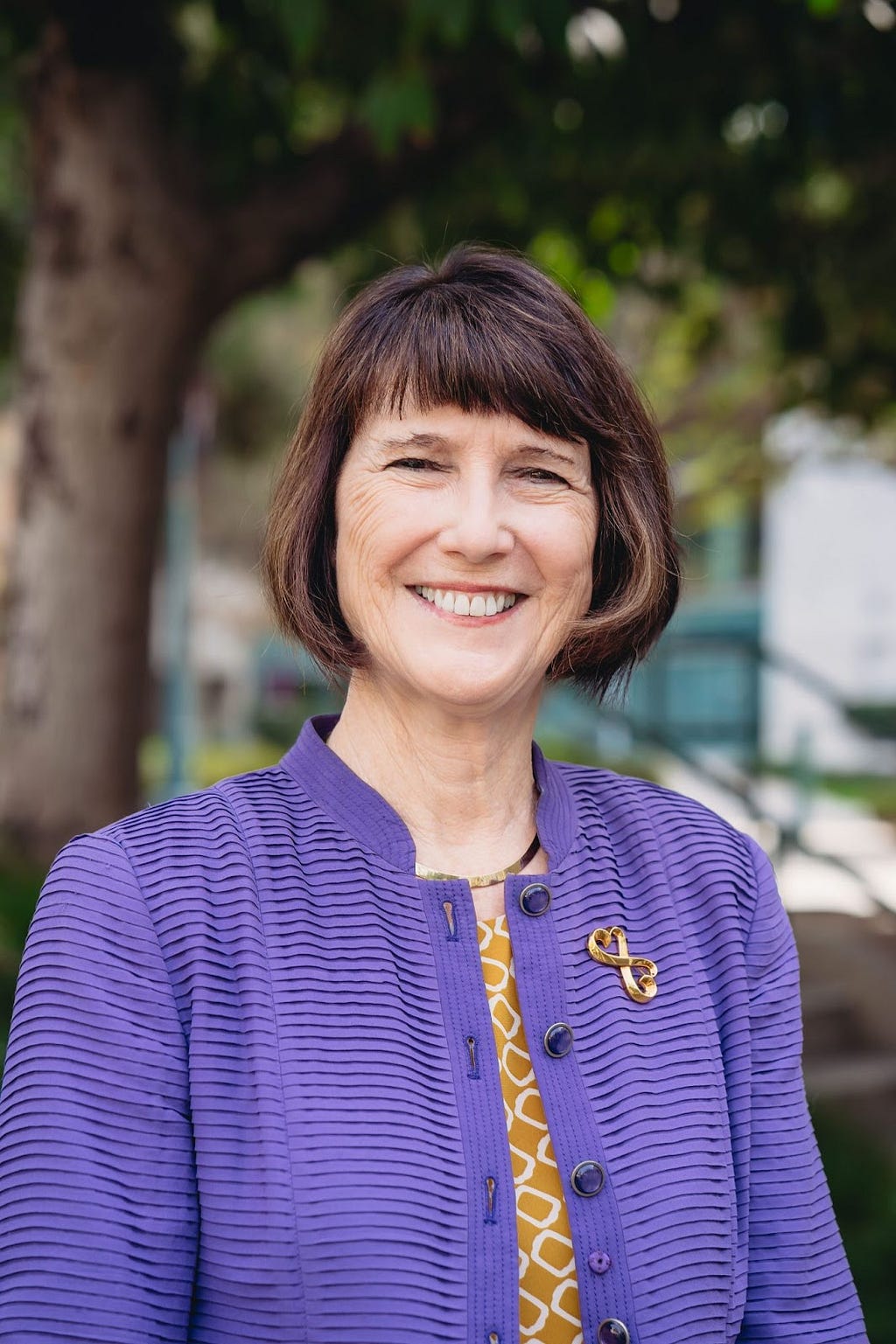 An image of President Dillon dresses in a purple cardigan wearing a golden heart pin. She is smiling at the camera.