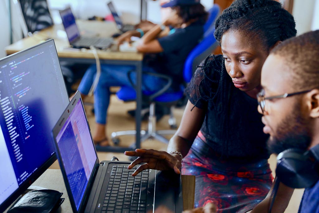 One female and one male looking focused and reviewing code on a laptop screen