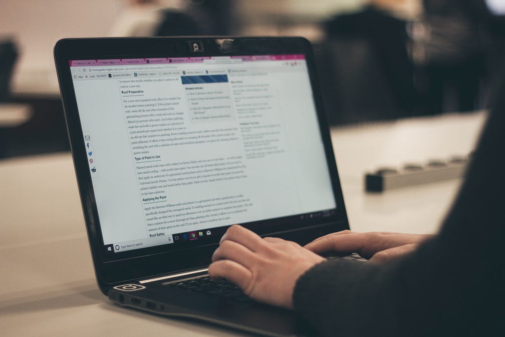 A man with only his hands visible typing a blog on his laptop.