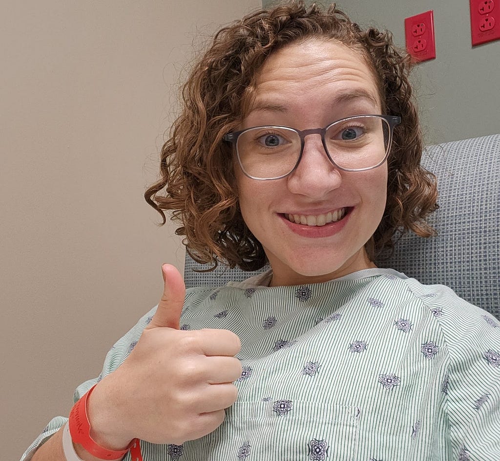 Woman in hospital giving thumbs up while wearing a hospital gown