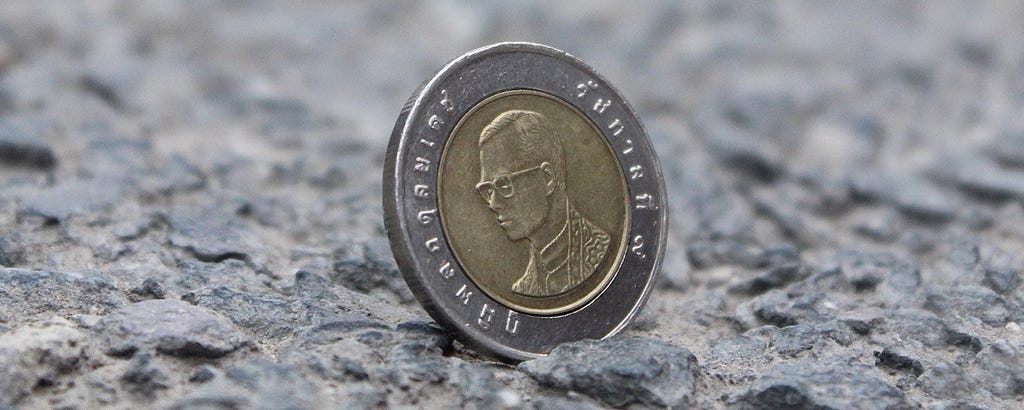 A coin with a head on it sits on a stone surface. The head is a man wearing glasses