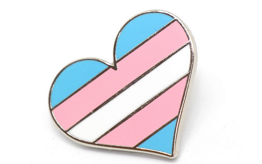 IMAGE DESCRIPTION: HEART PIN OF TRANSGENDER COLOR WITH BABY BLUE, PINK, AND WHITE STRIPES. PHOTO CREDIT: THE BRASS OWL.