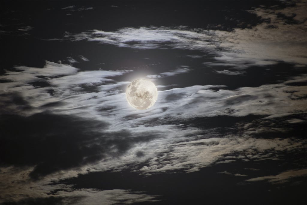 Lua cheia cercada de nuvens iluminando o céu.