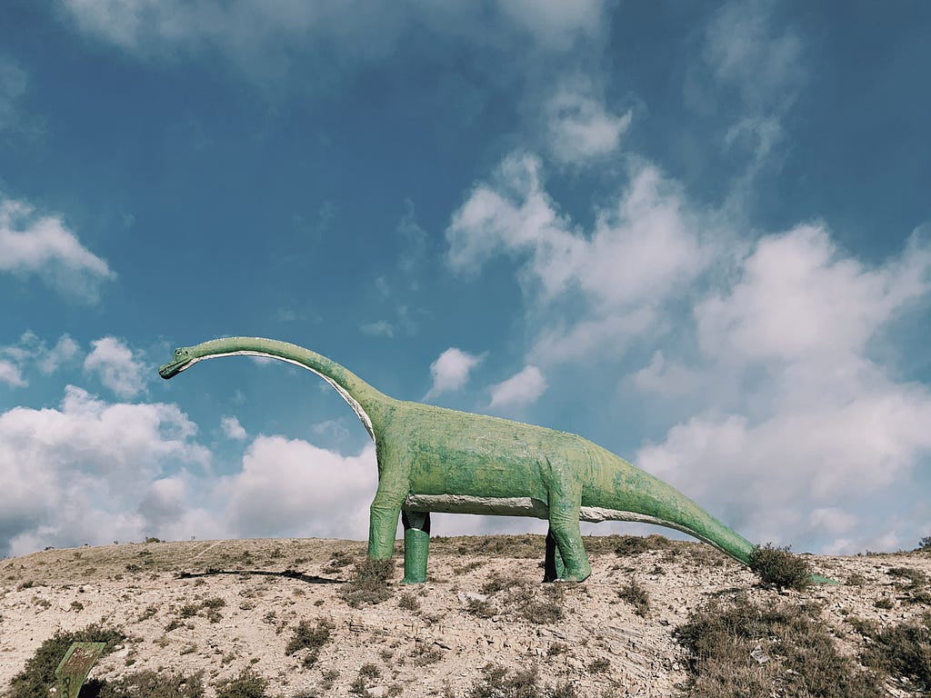 Model dinosaur standing on a hill with a blue sky in the background