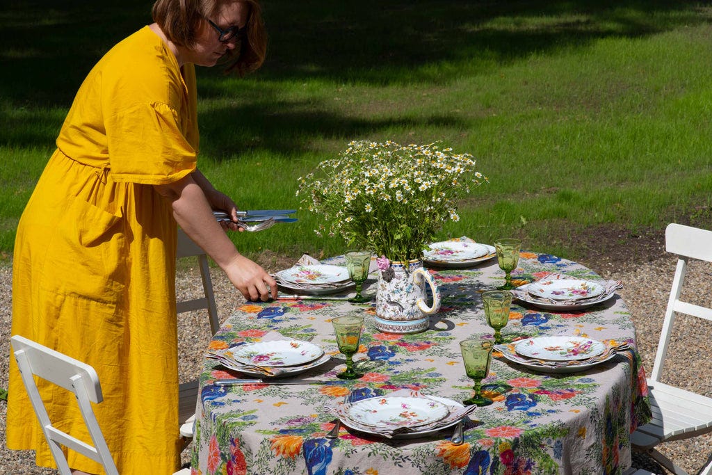 Sophie setting an outdoor table with floral plates, a colorful organic linen tablecloth and matching napkins.